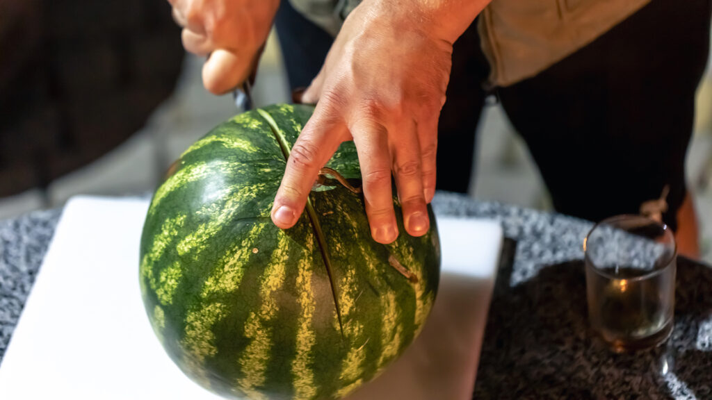 A man cuts a watermelon on a blurred kitchen backg 2023 11 27 04 52 26 utc